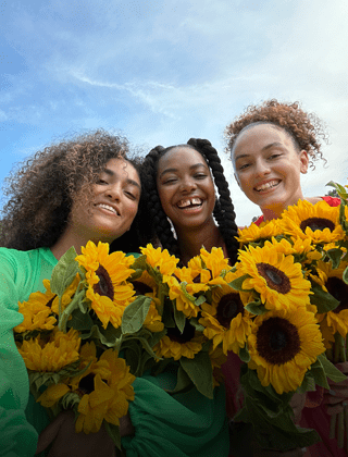 Selfie nítida e vibrante de três pessoas segurando flores.