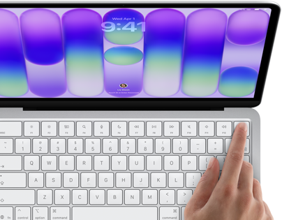 MacBook Neo prateado mostrando a tela de início de sessão, com o dedo de uma pessoa no sensor do Touch ID no canto superior direito do teclado